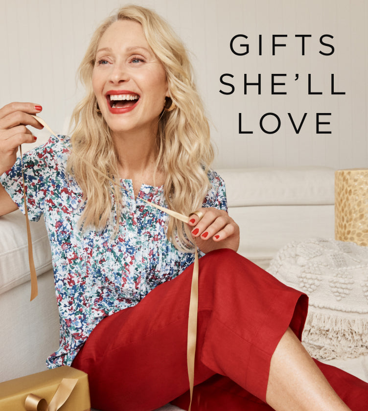 Woman wearing floral blouse and red pants sitting on a couch with a gift box, holding a ribbon, with text 